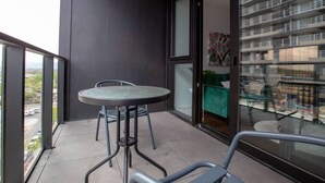 A balcony with a round table and chairs, a green sofa, and a view of a building with balconies. - Perfect Location 2 Bdrs Apartment@glen Waverley (Glen Waverley)