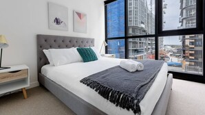 A modern hotel room with a large bed, a nightstand, a lamp, and a view of a construction site through the window. - Perfect Location 2 Bdrs Apartment@glen Waverley (Glen Waverley)