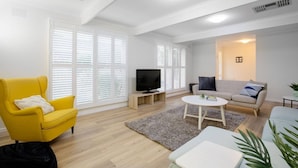 Una sala de estar moderna con un sillón amarillo, un sofá gris, un televisor y una mesita.