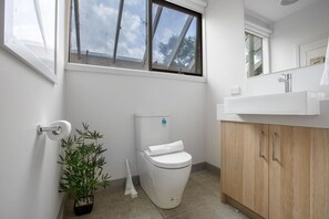 A bathroom with a toilet, a sink, a mirror, and a window. - Comfy Holiday House With Pool@rosanna (Rosanna)