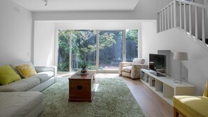 Una sala moderna con sofá, sillón, mesa de centro, televisor y una escalera.