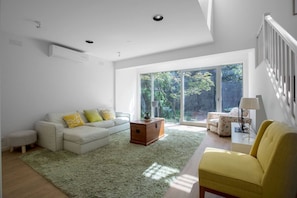 Uma sala de estar moderna com um sofá, poltronas, uma mesa de centro e vista para um jardim através de grandes portas de vidro deslizantes.