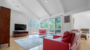 Un salón amplio con un gran ventanal, un televisor de pantalla plana, una mesa de centro de vidrio y un sofá de cuero rojo.