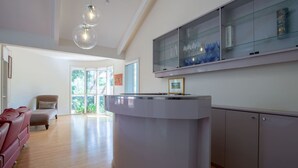 Una cocina moderna con una isla central, armarios con puertas de vidrio y un comedor con sofá rojo.
