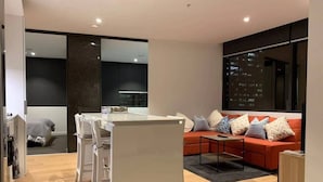 A modern living room with a sofa, a dining table, and a kitchen area. - Cozy Gem With Poolgym in Mel Cbd@southerncross (Melbourne)