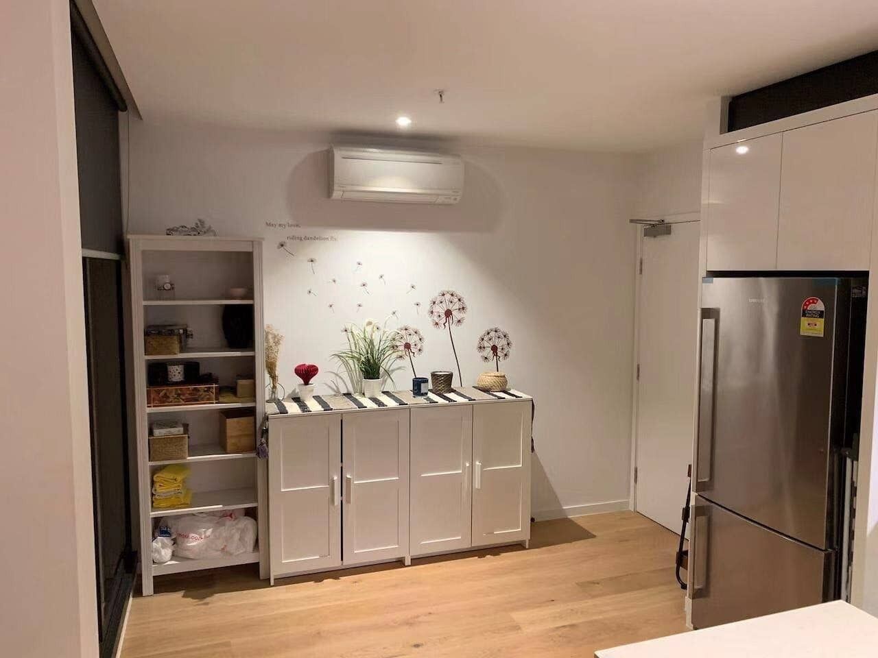 Une cuisine moderne avec des meubles blancs, un réfrigérateur en acier inoxydable et une étagère intégrée agrémentée d’objets décoratifs.