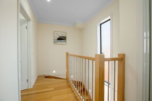 A hallway with wooden flooring, a wooden railing, and a painting on the wall.