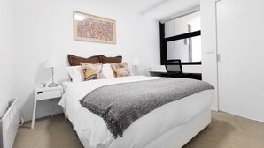 A bedroom with a bed, a nightstand, a desk, and a window. - Hawthorn Elegant Lifestyle 1 Bedroom Apartment (Hawthorn)