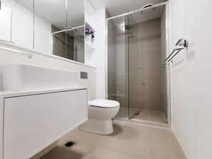Moderni kylpyhuone, jossa on wc, lasinen suihkuseinä ja valkoinen allaskaappi.