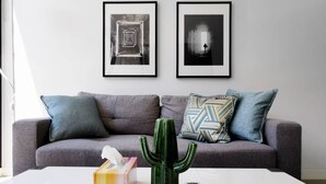A modern living room with a grey sofa, patterned cushions, a cactus, a tissue box, and a remote control on a white coffee table. Two framed artworks are hung on the wall above the sofa. - Hawthorn Elegant Lifestyle 1 Bedroom Apartment (Hawthorn)