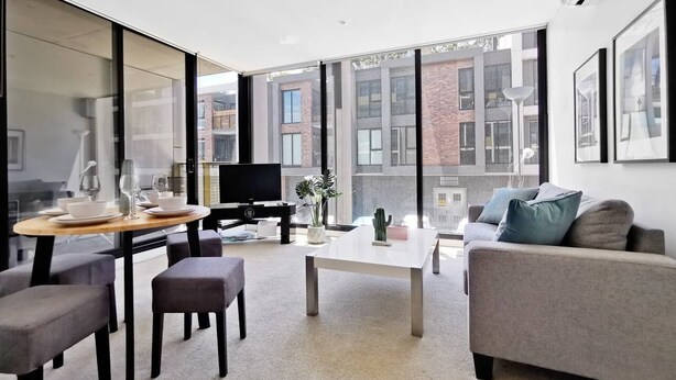 A modern living room with a sofa, a dining table, and a TV. - Hawthorn Elegant Lifestyle 1 Bedroom Apartment (Hawthorn)