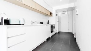 A modern kitchen with white cabinetry, a built-in oven, and a dark tiled floor. - Hawthorn Elegant Lifestyle 1 Bedroom Apartment (Hawthorn)