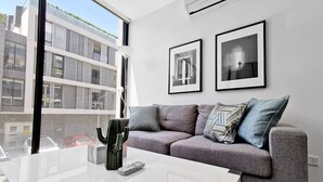 A modern living room with a grey sofa, two framed pictures, a cactus, and a remote control on a white coffee table. - Hawthorn Elegant Lifestyle 1 Bedroom Apartment (Hawthorn)