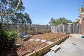 A backyard with a wooden fence, a bench, raised garden beds, and a paved area. - Peaceful Designer 2br@leafy Mill Park (Mill Park)