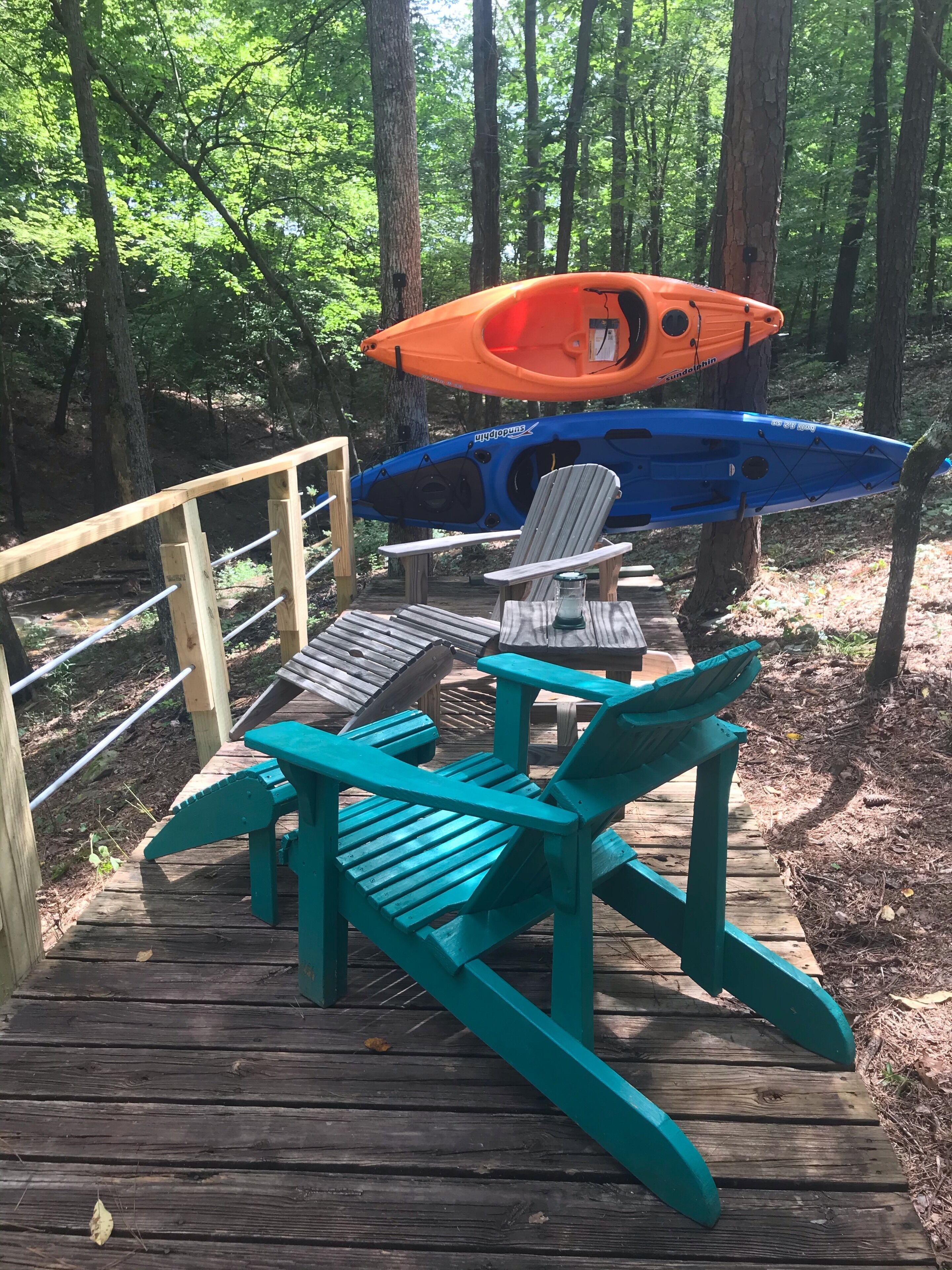 A wooden deck with two Adirondack chairs and a kayak rack holding two kayaks.