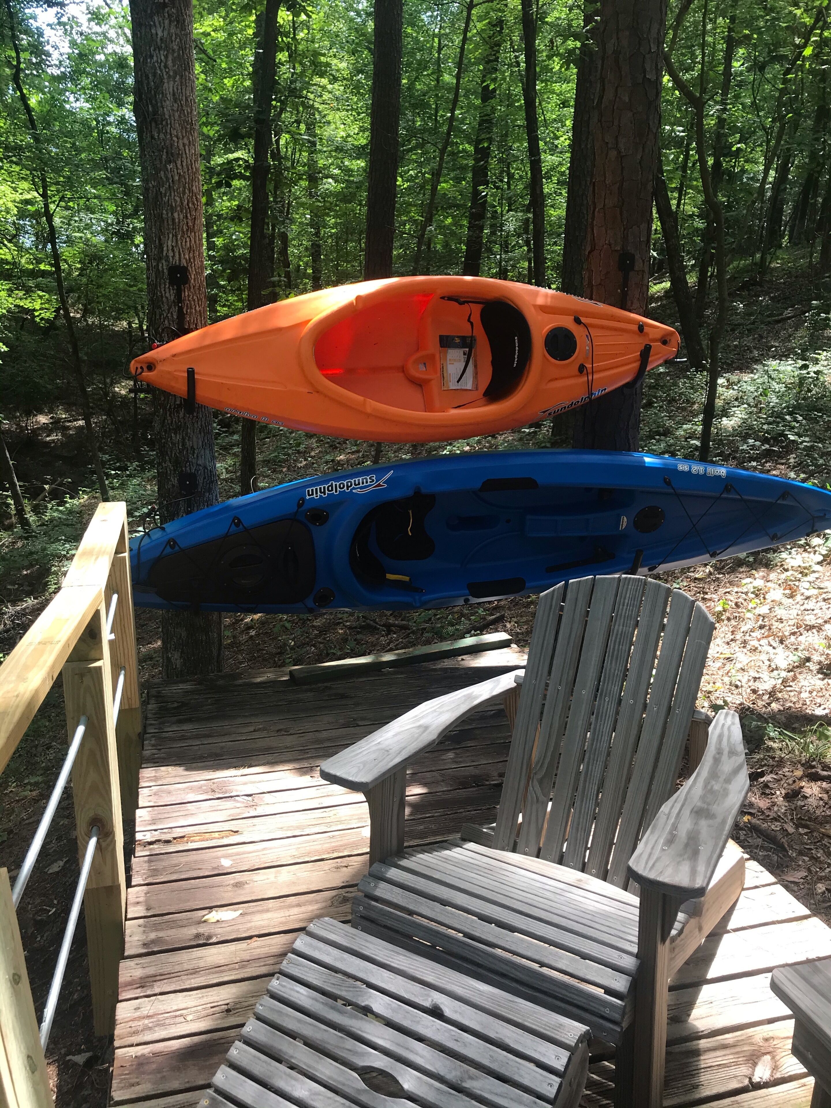 Deux kayaks, l’un orange et l’autre bleu, sont posés sur une terrasse en bois, à côté d’une chaise.