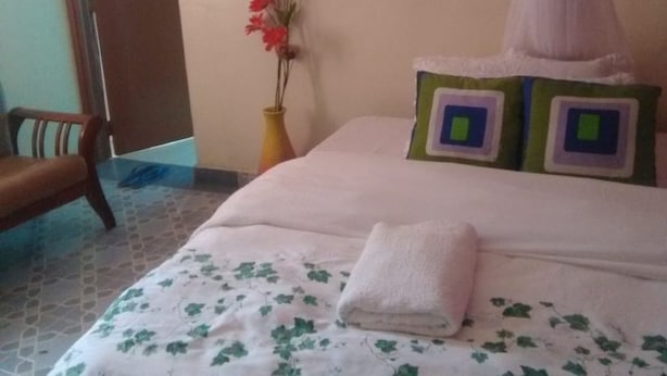 A bedroom with a bed, a chair, a painting, a vase with flowers, and a door.