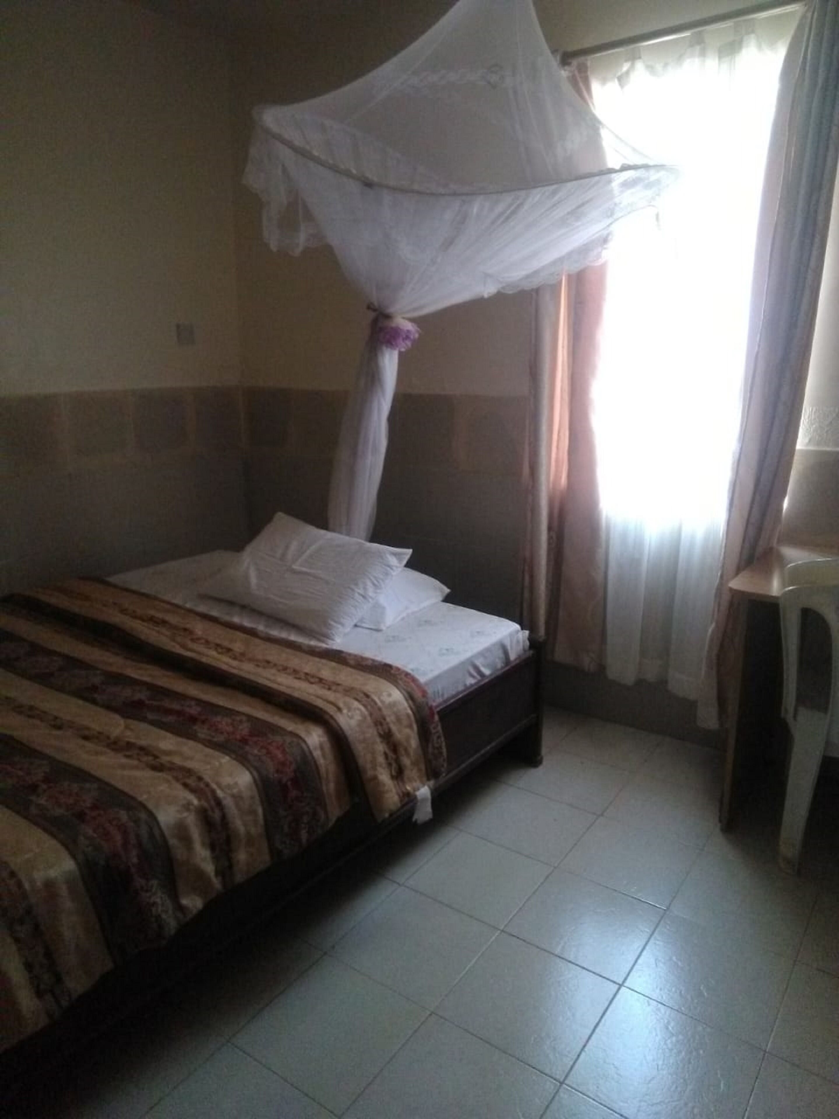 Un lit simple avec un baldaquin, une table de chevet et une fenêtre avec des rideaux.