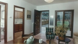 A spacious living room with a dining area, a kitchen, and a large window offering a view of the outdoors.
