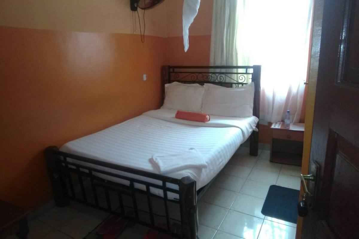 A single bed with a metal frame, white bedding, and a red pillow.