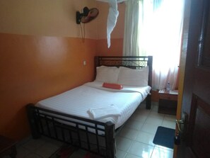 Un lit simple avec un cadre en métal, du linge de lit blanc et un oreiller rouge.
