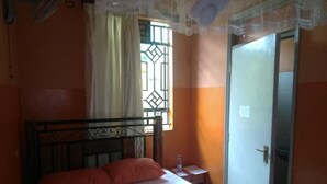 Una cama individual con cabecera, una mesita de noche, una ventana con reja de metal y una puerta.