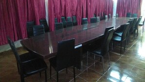 Un salón de conferencias con una larga mesa y sillas, cortinas rojas y suelo de baldosas.
