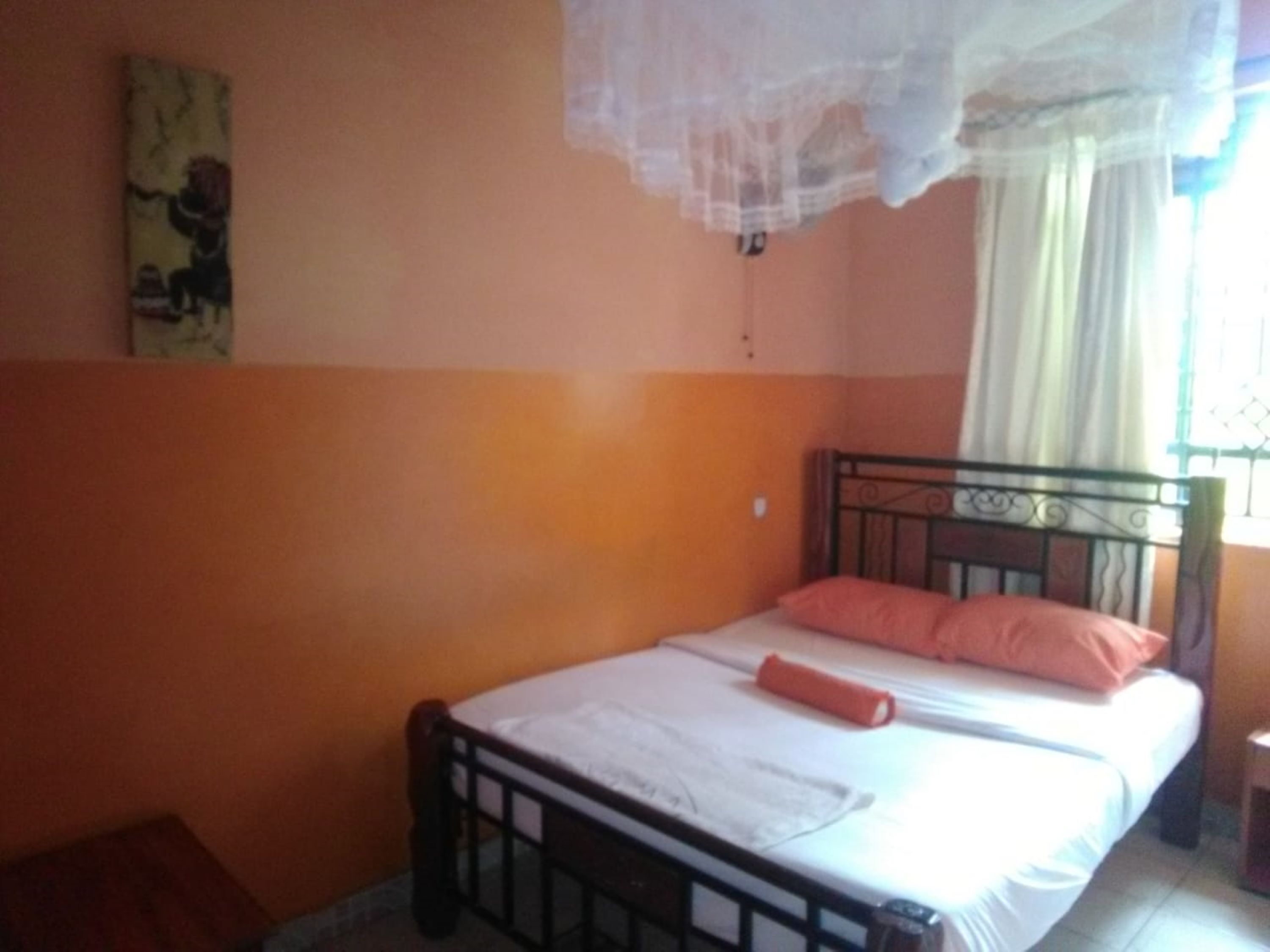 A bedroom with a bed, a nightstand, a window with curtains, and a wall with a painting.