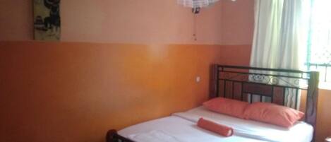 A bedroom with a bed, a nightstand, a window with curtains, and a wall with a painting.