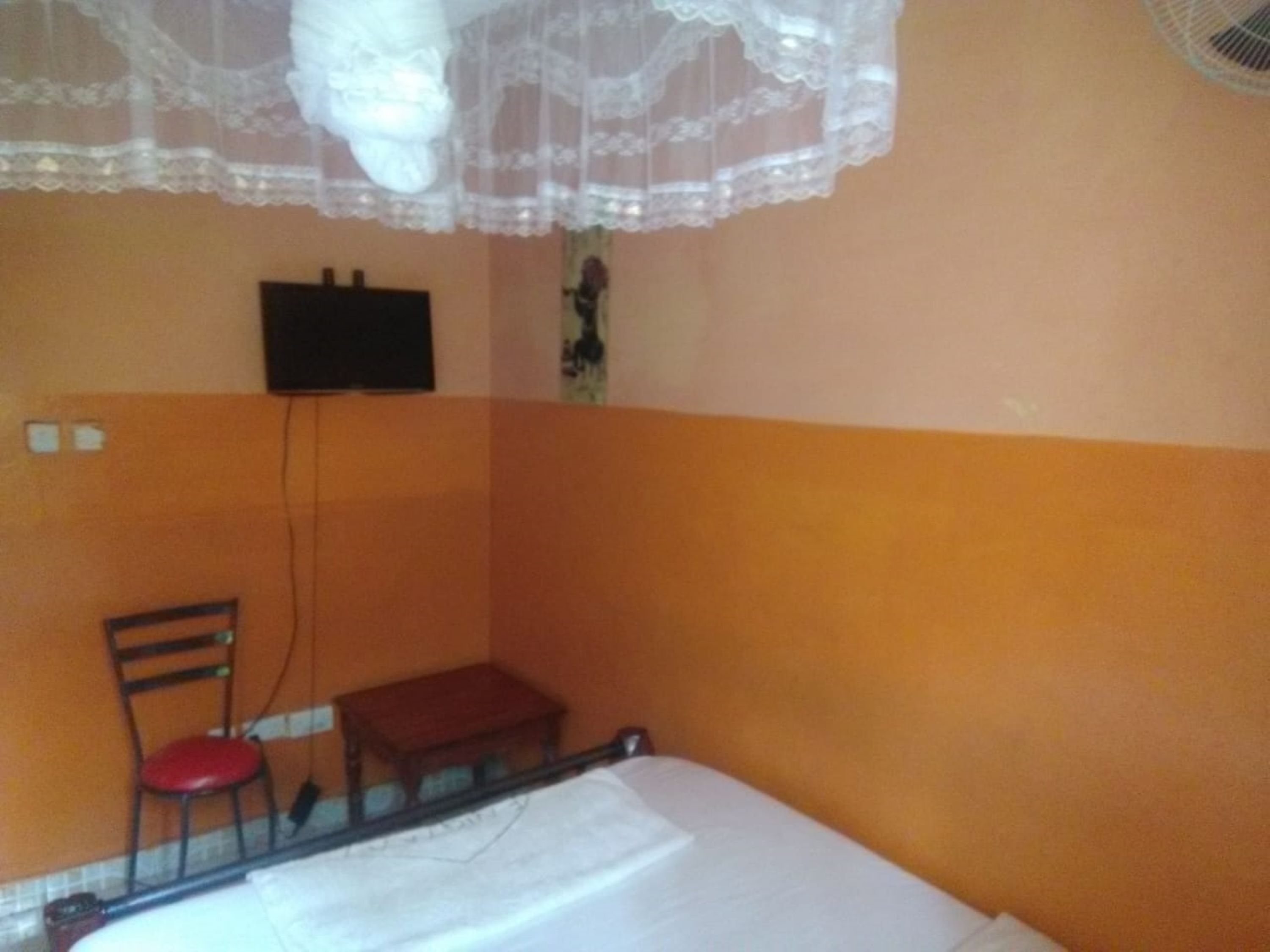 A room with a bed, a chair, a small table, and a TV mounted on the wall.