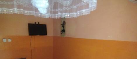 A room with a bed, a chair, a small table, and a TV mounted on the wall.
