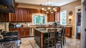 A spacious kitchen with wooden cabinets, a granite island, and a chandelier. - Large Luxury Family Home Near Five Colleges. The TOP short term rental in area! (Hadley)