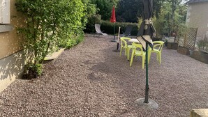 An outdoor patio area with a gravel surface, surrounded by greenery and trees. - Cozy 1-Bedroom Apartment Near Saint Roch Thermal Baths, La Roche-Posay (La Roche-Posay)
