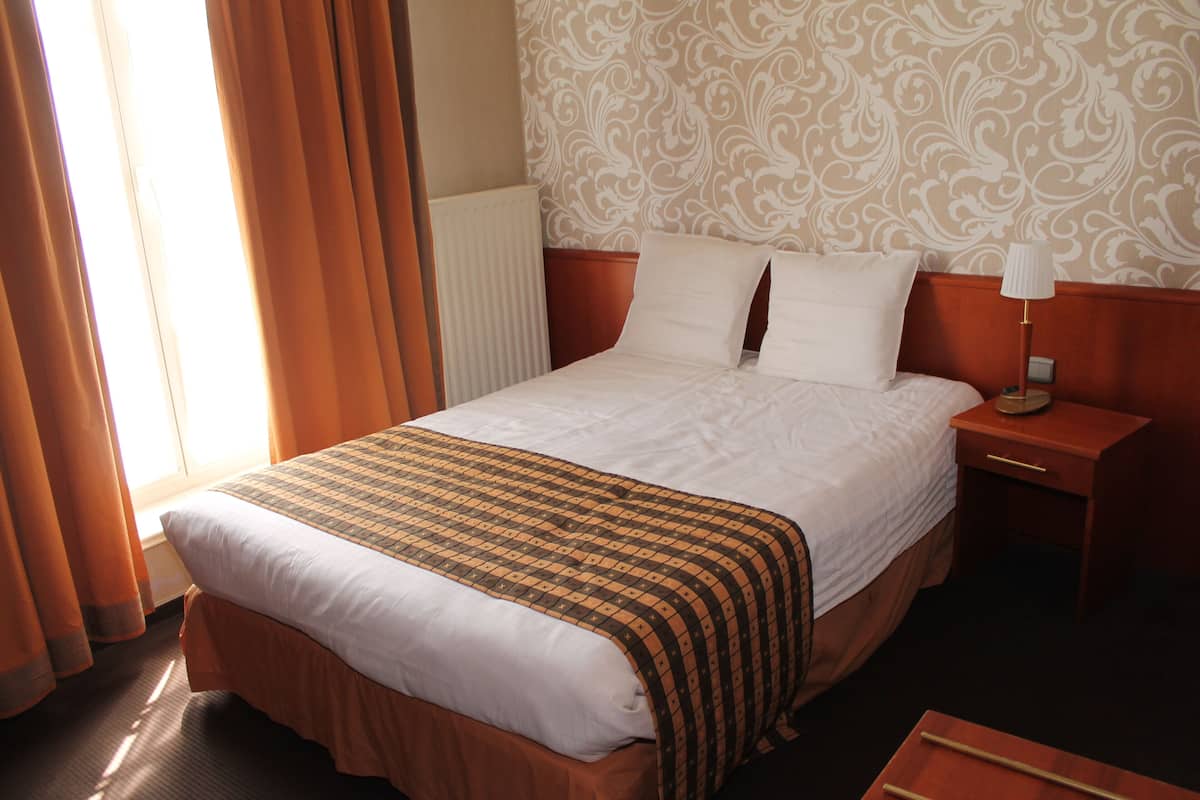 A hotel room with a large bed, a nightstand, a lamp, and a window with curtains.
