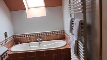 A bathroom with a bathtub, a towel rack, and a skylight.