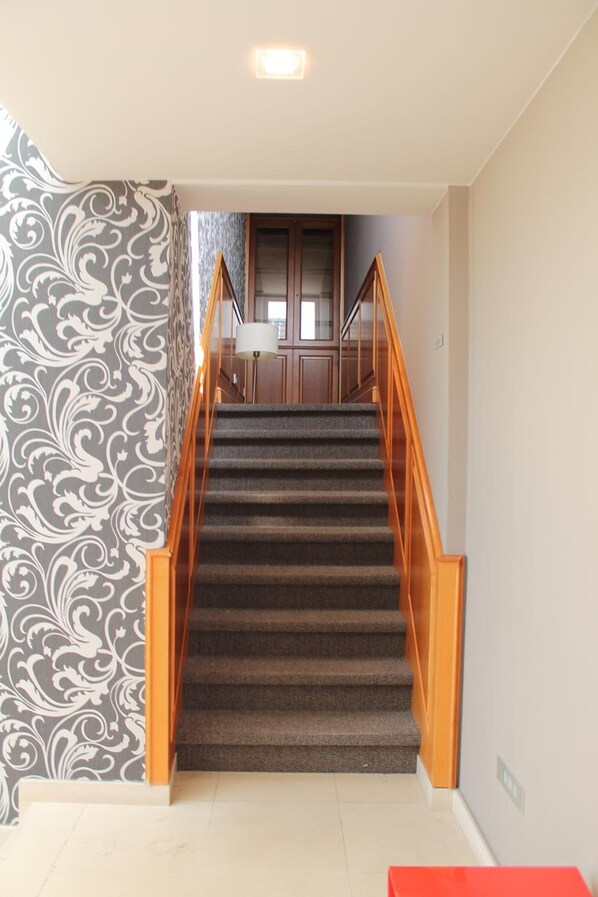 Una escalera con peldaños alfombrados, barandillas de madera y un papel tapiz estampado a la izquierda.