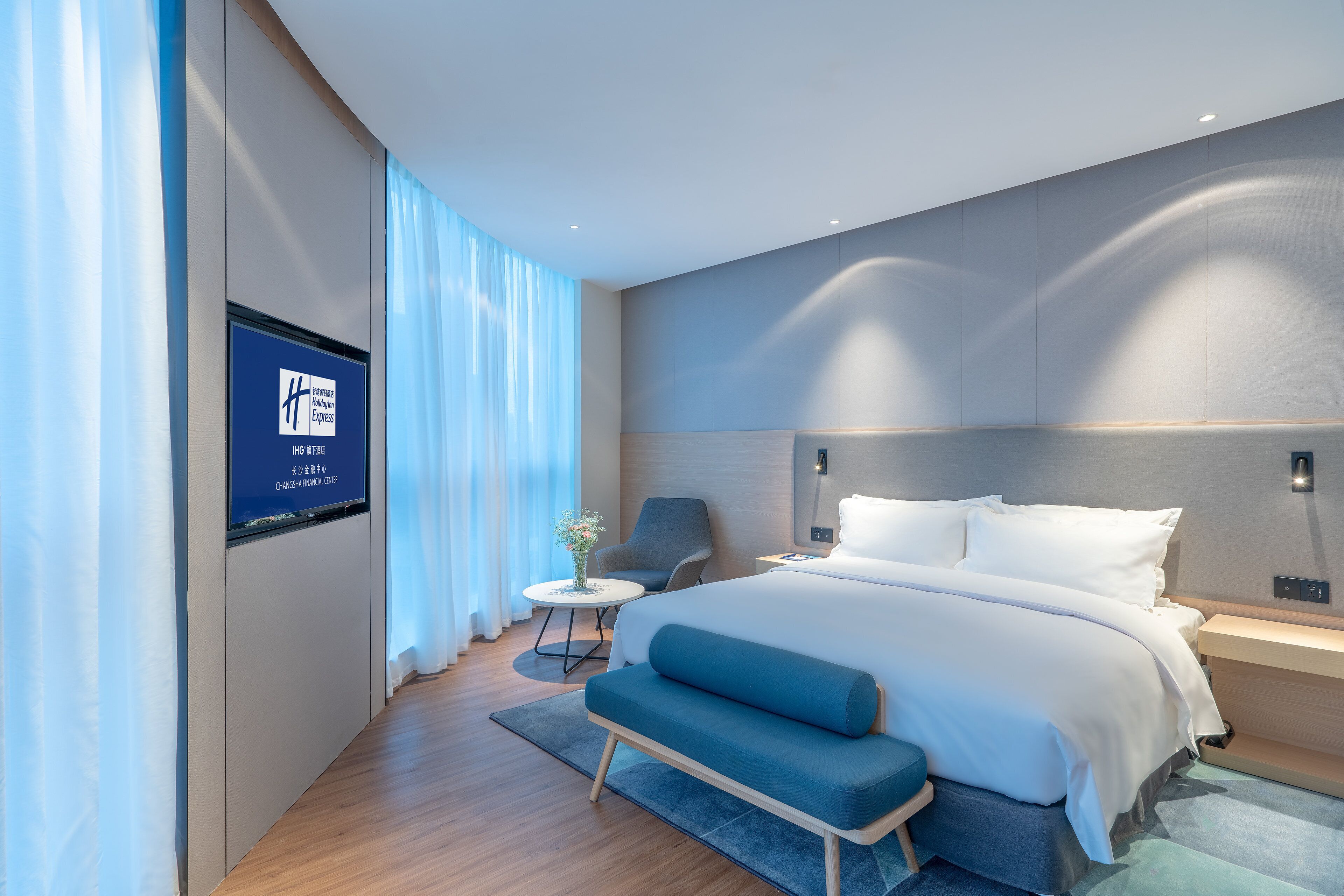 Habitació d'hotel moderna amb un llit gran, una taula de treball, una cadira i una televisió penjada a la paret.