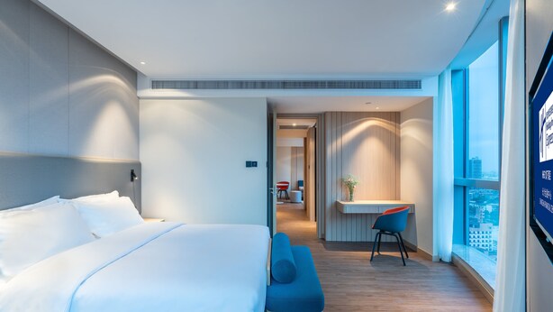 Quarto de hotel moderno com uma cama grande, uma escrivaninha e vista para a cidade.