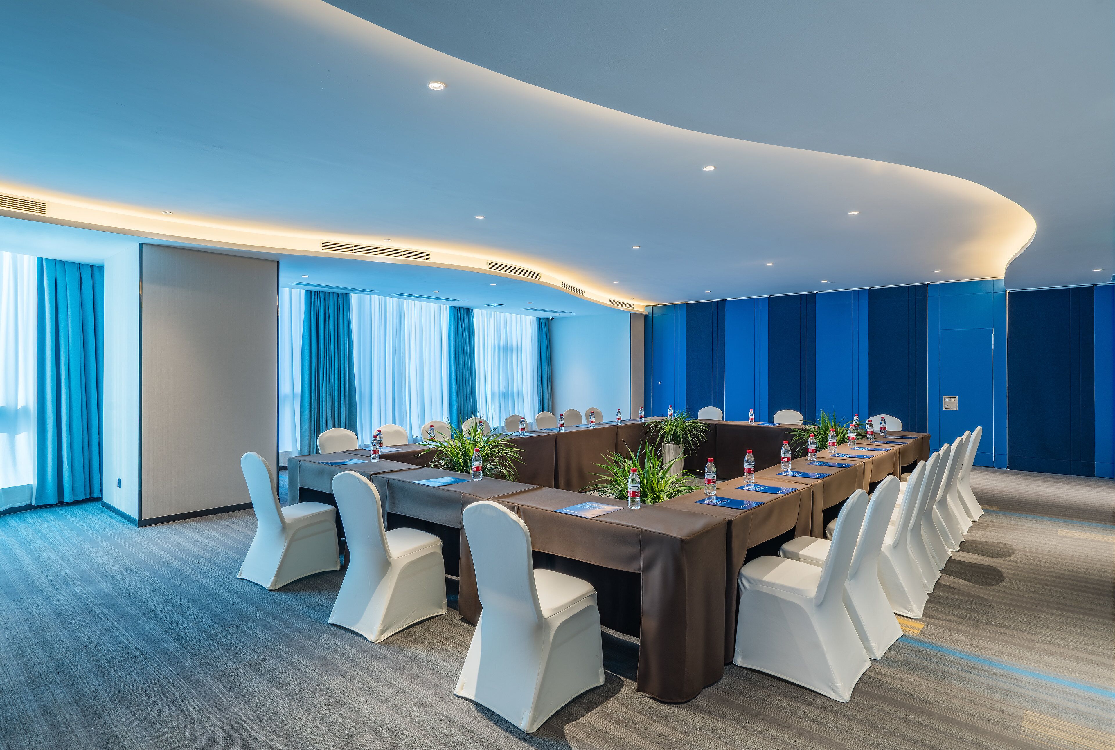 Une salle de conférence avec une longue table, des chaises blanches et des rideaux bleus.