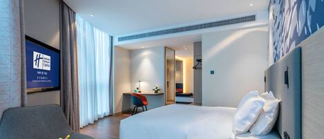 A hotel room with a bed, a desk, a chair, a small table with fruit, and a TV displaying hotel information.