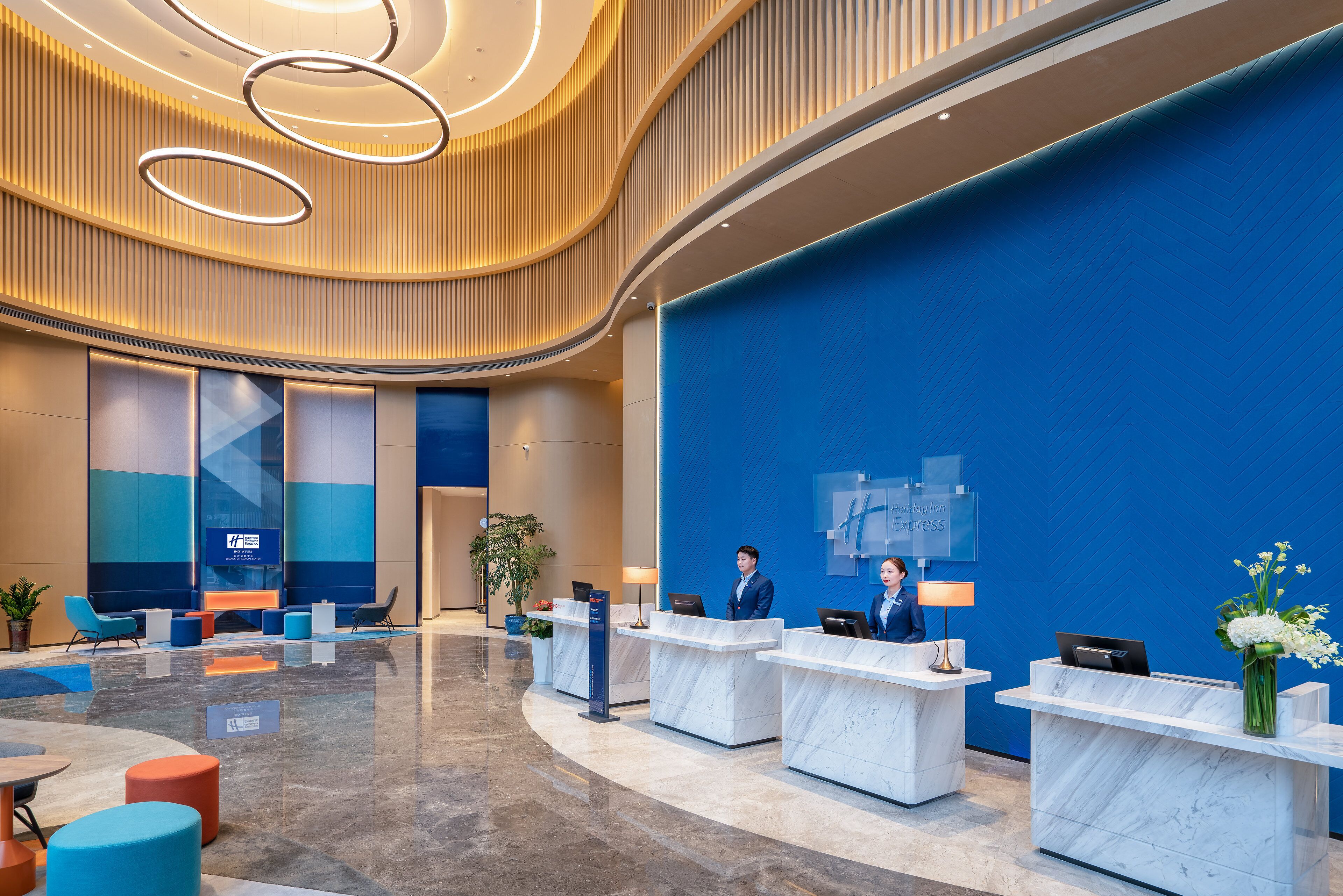 A modern hotel lobby with marble reception desks, seating areas, and a large blue wall.