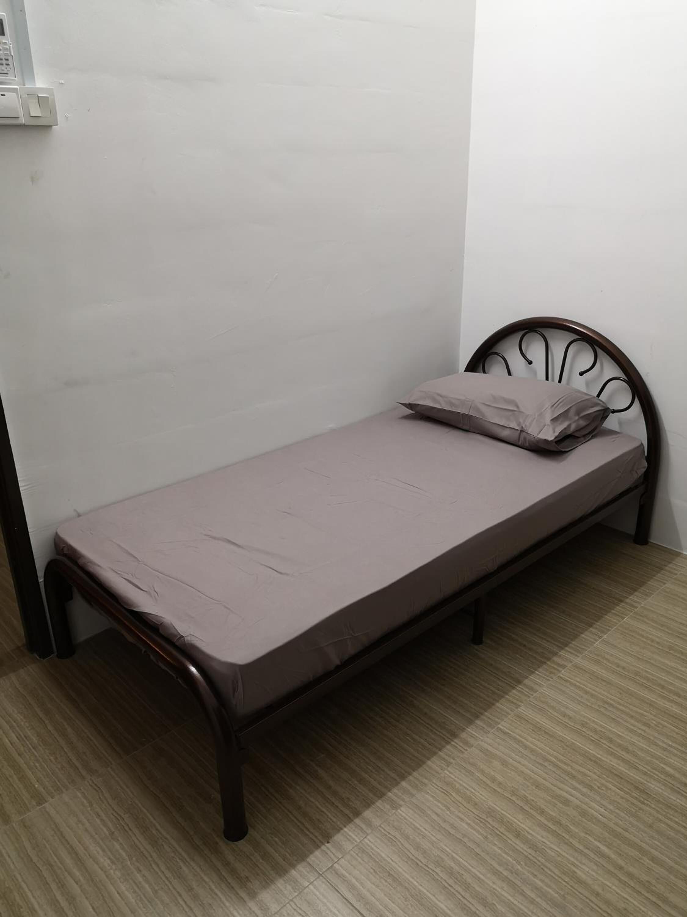 A small, single-bed room with a metal frame, a plain mattress, and a single pillow.