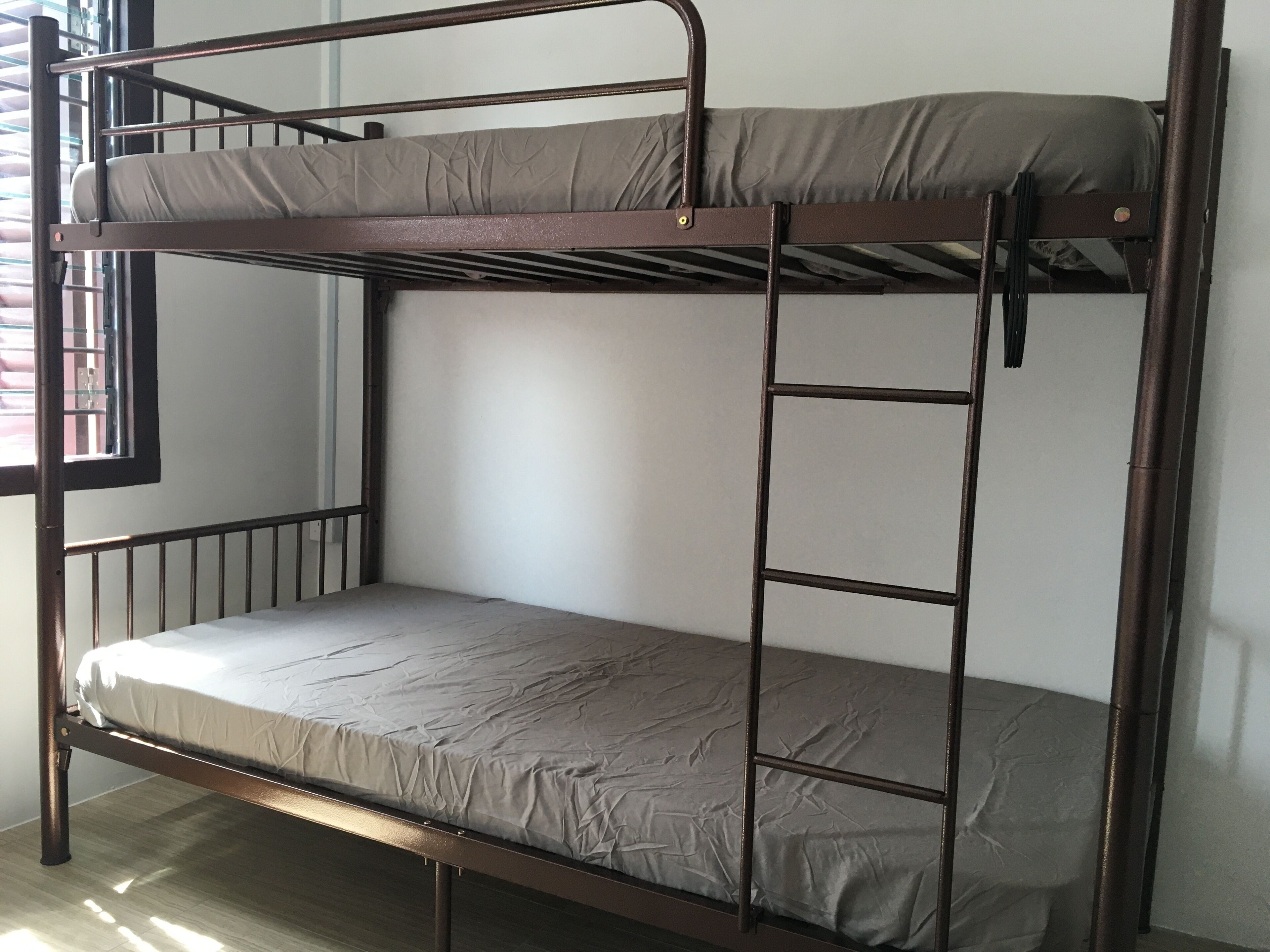 Una cama litera con escalera, una ventana con barrotes y una pared lisa.
