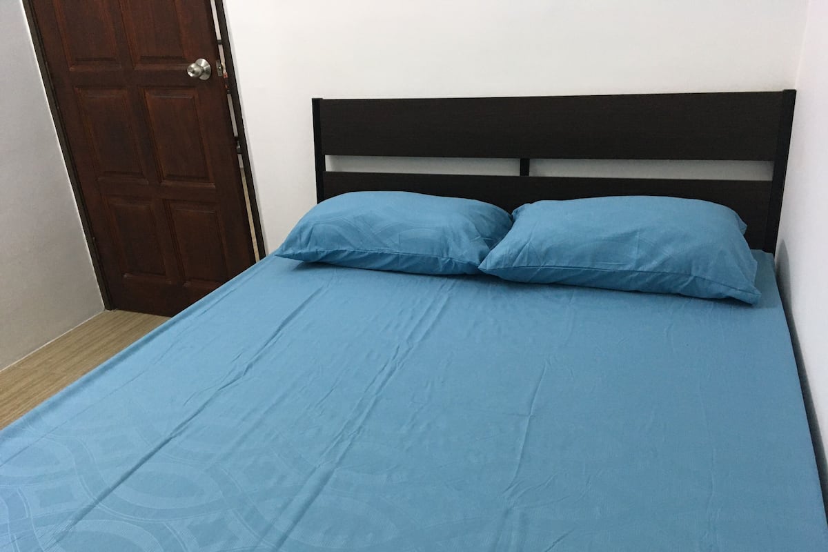 A bed with a blue bedspread and two pillows, a wooden headboard, and a closed door.