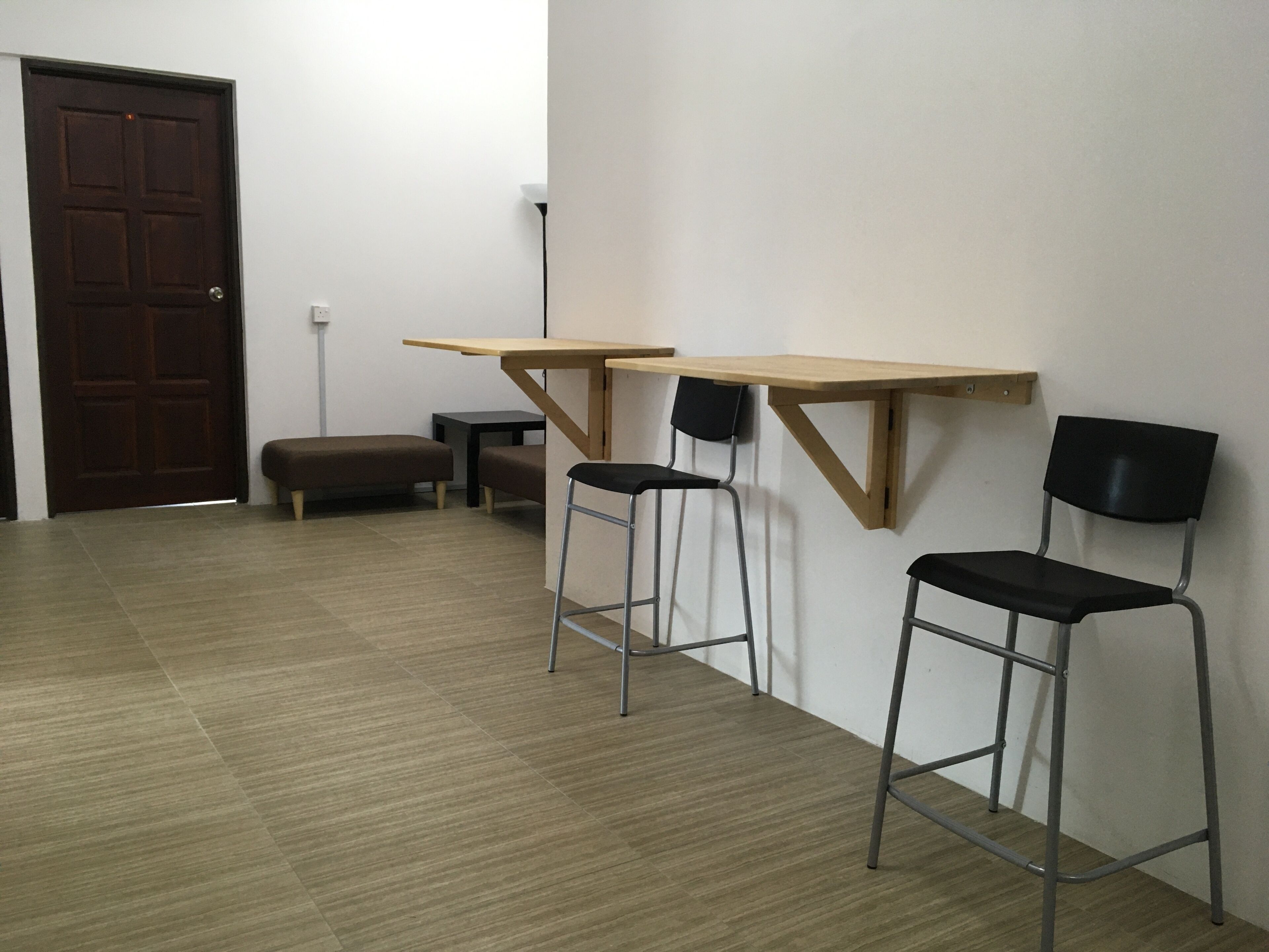 Une pièce comprenant deux tables en bois, deux chaises noires, un banc et une porte.