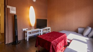 Habitación de hotel con cama, televisión, mesa con mantel rojo, calentador portátil y un reloj en la pared.