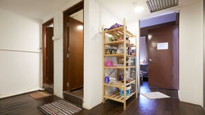 Un pasillo con piso de madera, un estante de madera con varios objetos, y una puerta con un letrero.