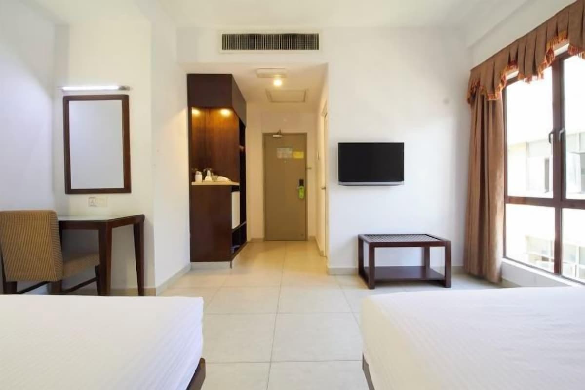 A hotel room with two beds, a desk, a chair, a TV, and a bathroom visible through an open door.