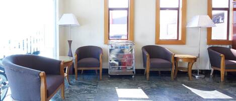 A lobby with four armchairs, a small table, a lamp, and a magazine rack.
