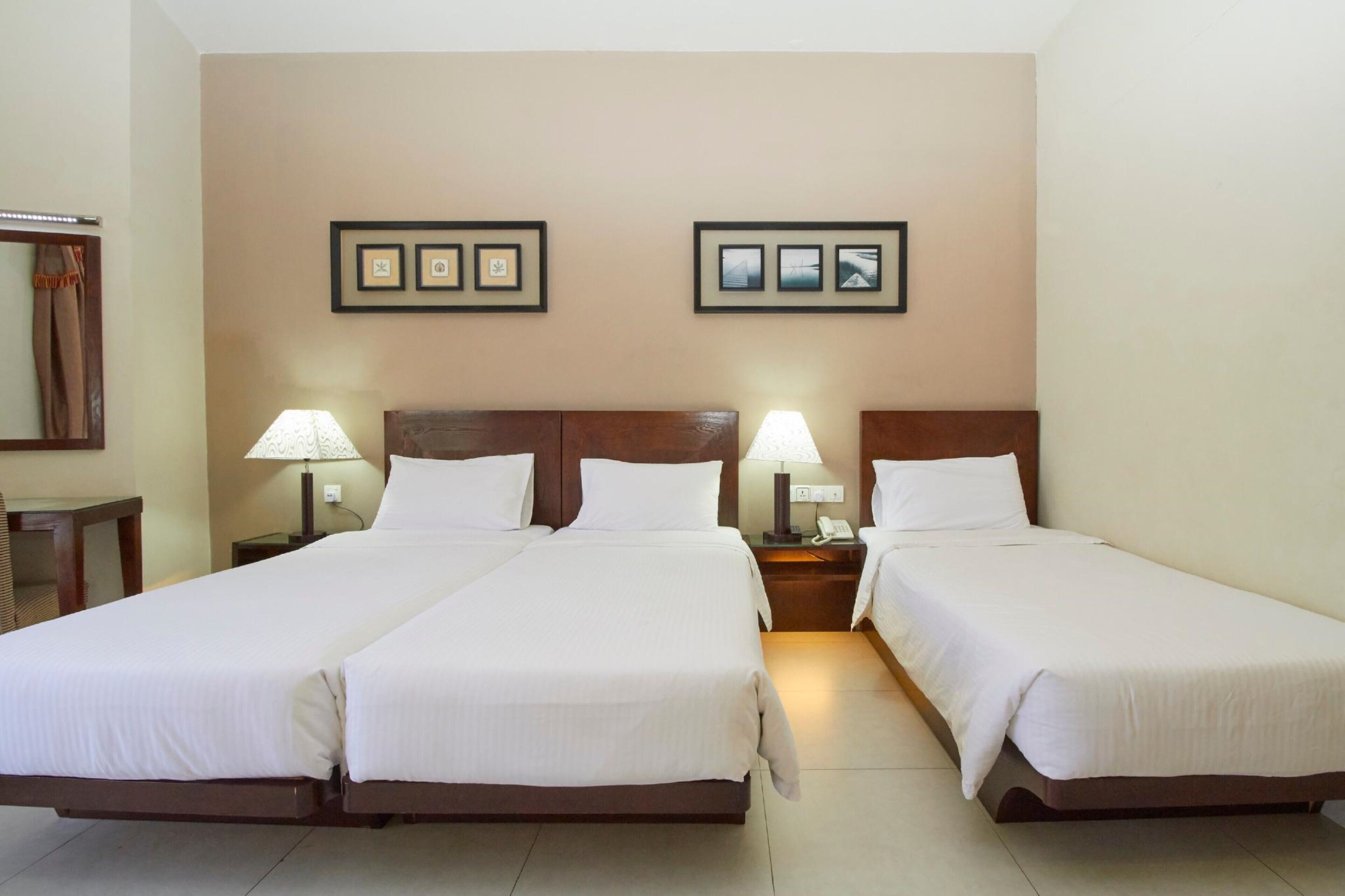 A hotel room with two single beds, a wooden headboard, bedside lamps, and framed pictures on the wall.